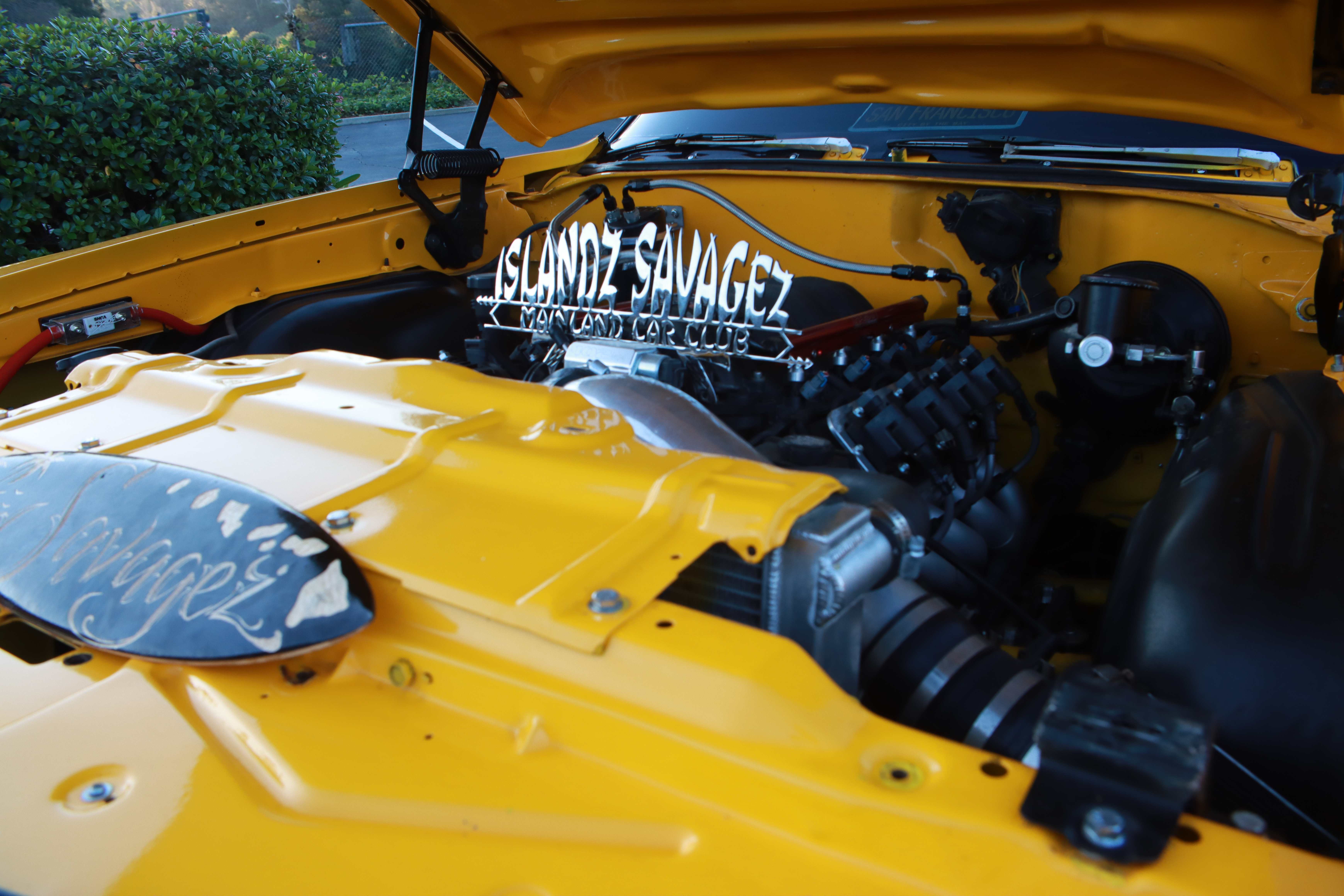 Yellow Oldsmobile Cutlass engine bay with Islandz Savagez Mainland Car Club banner
