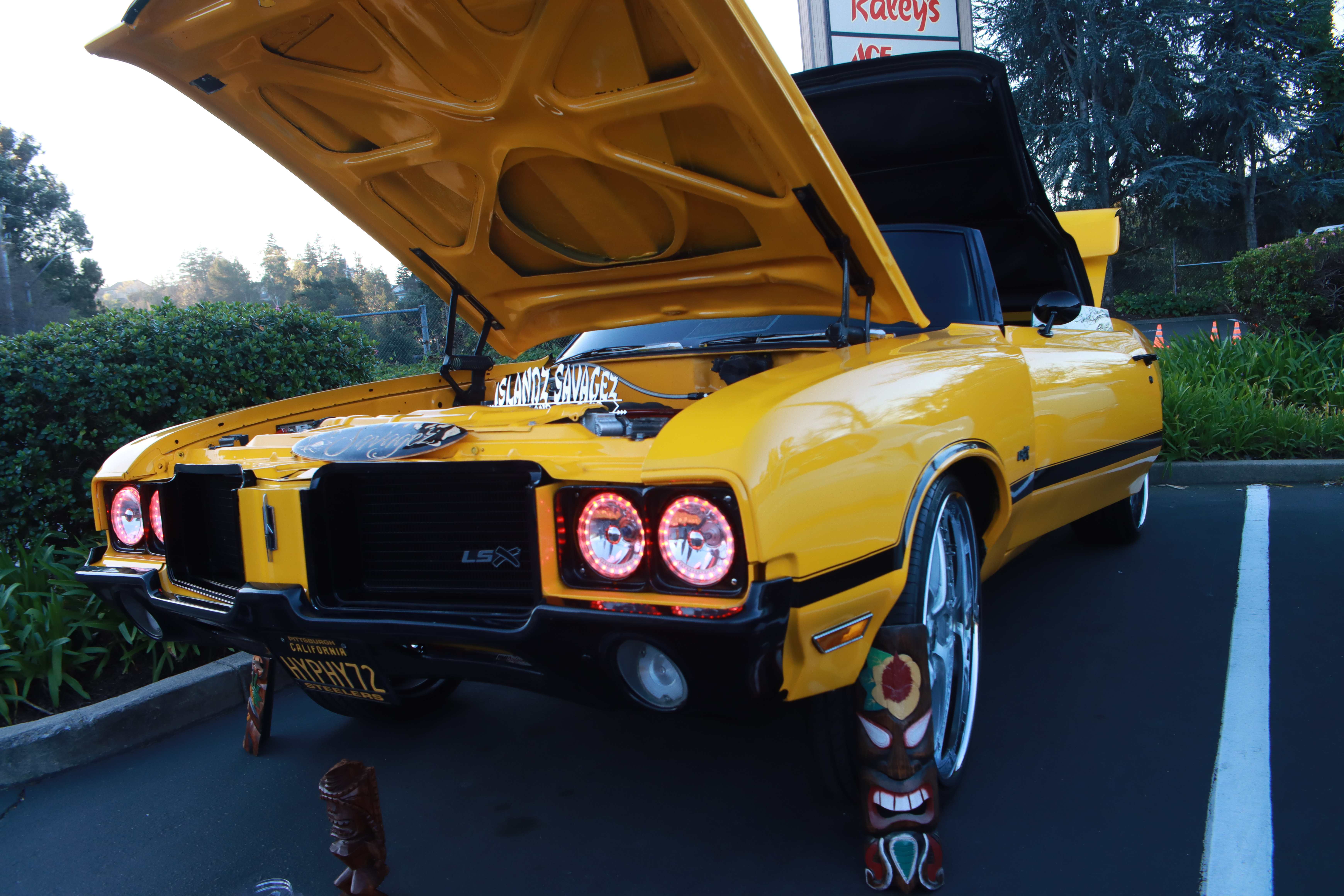 Yellow Oldsmobile Cutlass rear view with tiki decoration and Islandz Savagez graphics