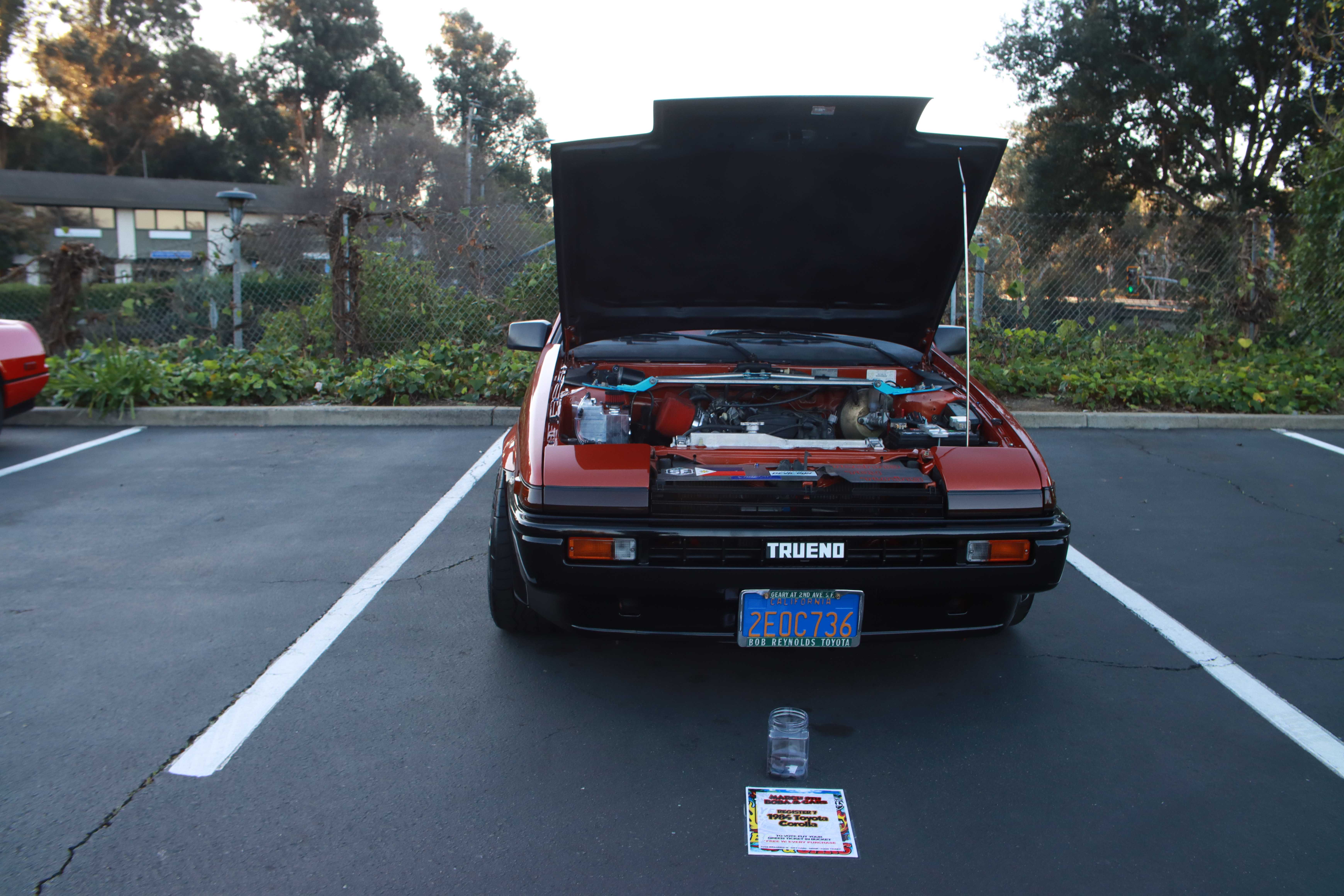 Red Toyota AE86 Corolla Trueno head-on view with voting jar on pavement